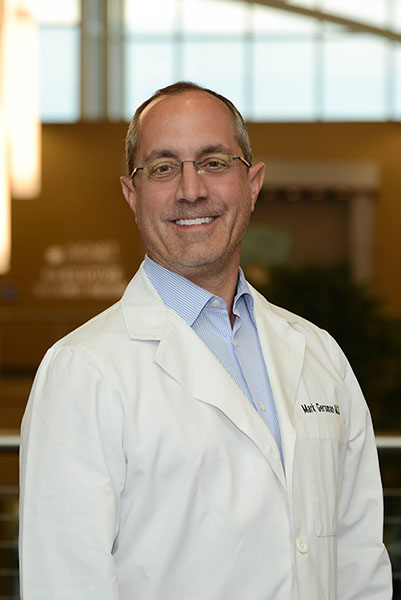 A man in white lab coat standing next to a railing.